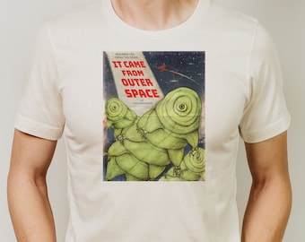 May include: A white t-shirt featuring a vintage-style illustration of green alien creatures from outer space. The text "It Came From Outer Space" is printed in red on the shirt.