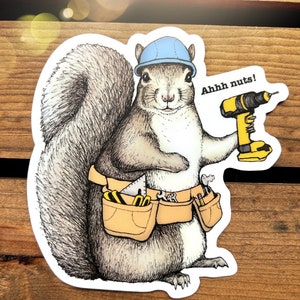 Peut inclure: Un &eacute;cureuil de dessin anim&eacute; portant un casque bleu et une ceinture &agrave; outils avec une perceuse dans sa main. L'&eacute;cureuil dit "Ahhh nuts!"