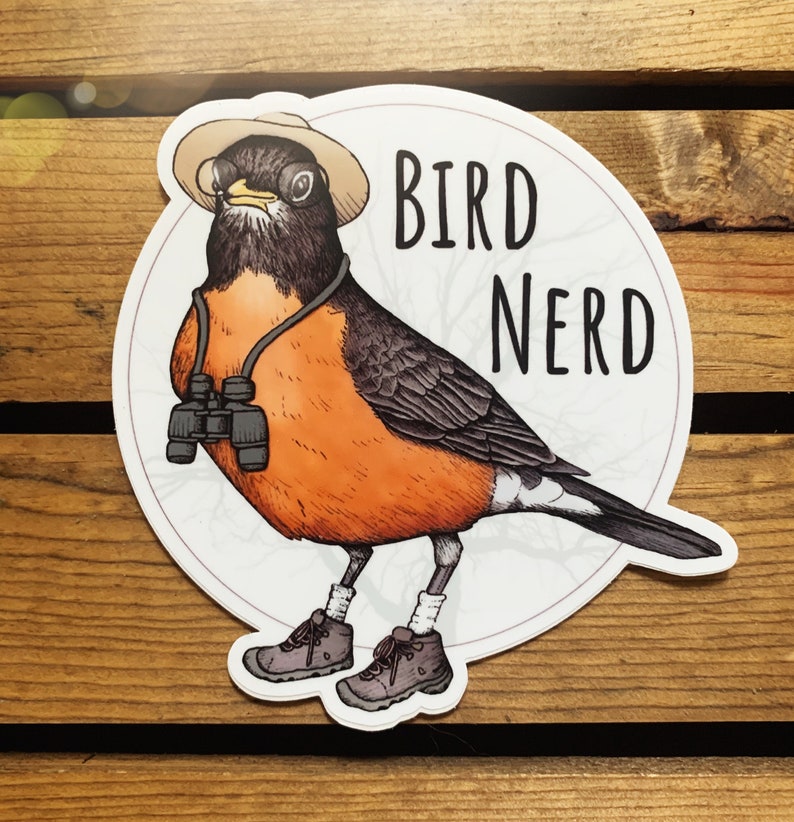May include: A sticker featuring a cartoon robin wearing a hat and glasses, holding binoculars. The text "BIRD NERD" is written in black letters on a white background.