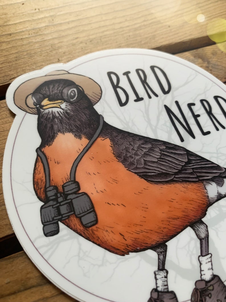 May include: A round sticker with a cartoon robin wearing a hat and binoculars. The robin is standing on a branch with the text "BIRD NERD" above it.