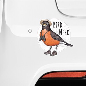 May include: A white car with a sticker of a cartoon robin wearing a hat, glasses, and binoculars. The sticker says "Bird Nerd".