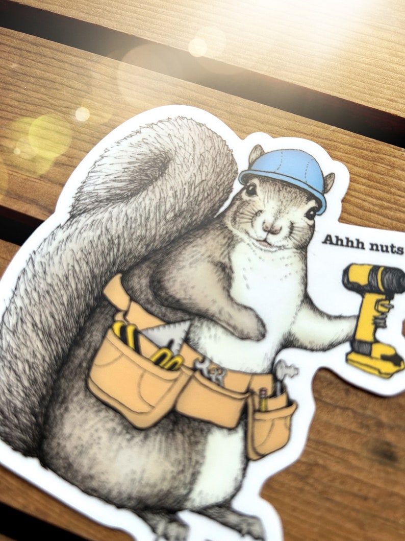 Peut inclure: Un &eacute;cureuil de dessin anim&eacute; portant un casque bleu et une ceinture &agrave; outils tient une perceuse jaune et noire. L'&eacute;cureuil regarde la perceuse et a une bulle de dialogue qui dit "Ahhh nuts".