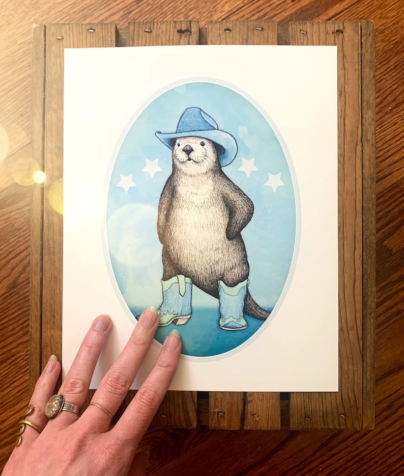 K&ouml;nnte beinhalten: Eine Cartoon-Illustration eines Otters, der einen blauen Cowboyhut und blaue Stiefel tr&auml;gt und auf einem blauen und wei&szlig;en Hintergrund mit wei&szlig;en Sternen steht.