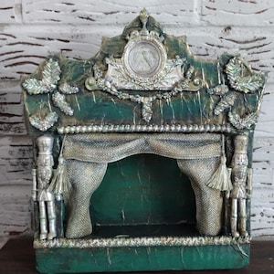 May include: A green and gold painted wooden puppet theater with a gold and white curtain and two nutcracker figurines on the sides.
