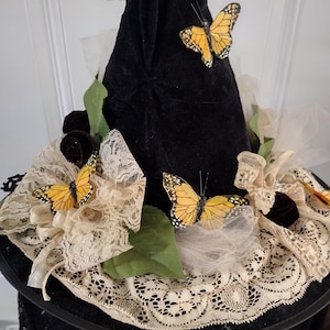 May include: Black velvet witch hat decorated with yellow and black butterflies, cream lace, and black roses. The hat has a wide brim and a tall, pointed crown, perfect for a costume or themed event.