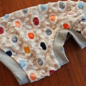 May include: A pair of gray and beige baby pants with a floral pattern. The pants have a gray elastic waistband and a white background with colorful flowers.
