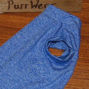May include: A blue pet shirt with a hole for the arm. The shirt is made of a soft, textured fabric. The words "Purr Wear" are visible on a wooden sign in the background.