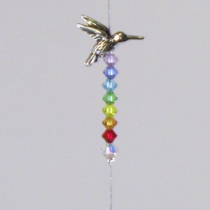 May include: A crystal suncatcher with a silver hummingbird charm and a rainbow of crystal beads hanging from it.