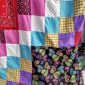 May include: A patchwork quilt made of various fabrics, including red, pink, blue, green, yellow, and purple. The quilt is made up of squares of different patterns, including polka dots, stripes, and paisley. The quilt is edged with a red fabric.