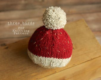 May include: A red and white knitted hat with a white pom-pom on top. The hat is sitting on a wooden surface. three...birds PDF Knitting Pattern
