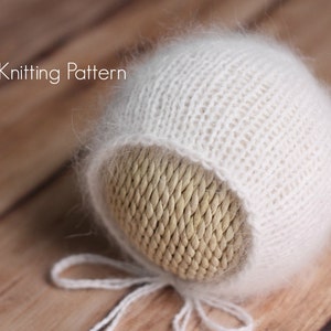 May include: White knitted baby hat with a fuzzy texture. The hat is tied with a white ribbon.