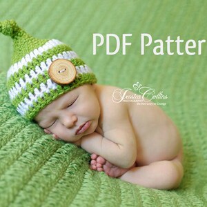 Könnte beinhalten: Eine grün-weiße Häkelmütze mit einem Holzknopf. Die Mütze liegt auf einem schlafenden Baby auf einer grünen Decke. PDF-Muster.