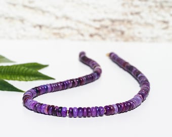 Könnte beinhalten: Eine Halskette bestehend aus zahlreichen kleinen, flachen, kreisförmigen Perlen in verschiedenen Schattierungen von tiefem Violett und Purpur. Die Perlen sind auf einem einzelnen Strang aufgereiht und haben eine glatte, polierte Textur.