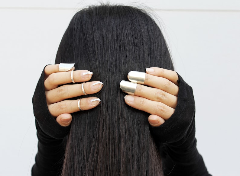 May include: A person wearing black fingerless gloves with silver rings on their fingers. The rings are different shapes and sizes.
