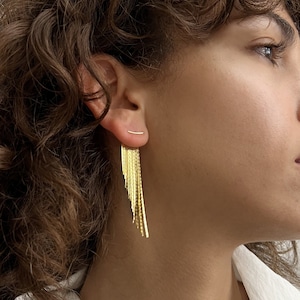 Puede incluir: Un par de pendientes de oro, uno con una cadena larga y fina de eslabones de oro y el otro con una barra corta y recta.