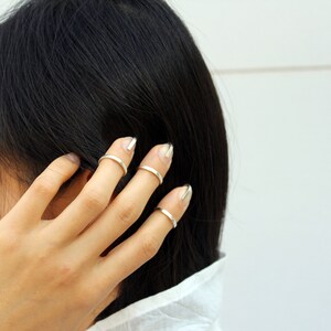 May include: A person's hand wearing multiple thin silver rings on their fingers. The rings are simple and minimalist in design.