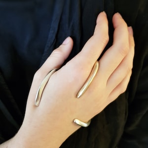 May include: A silver hand jewellery set with two curved pieces that wrap around the fingers and wrist.