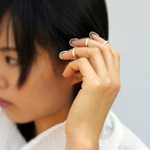 May include: A person wearing multiple silver rings on their fingers. The rings are open and wrap around the finger.