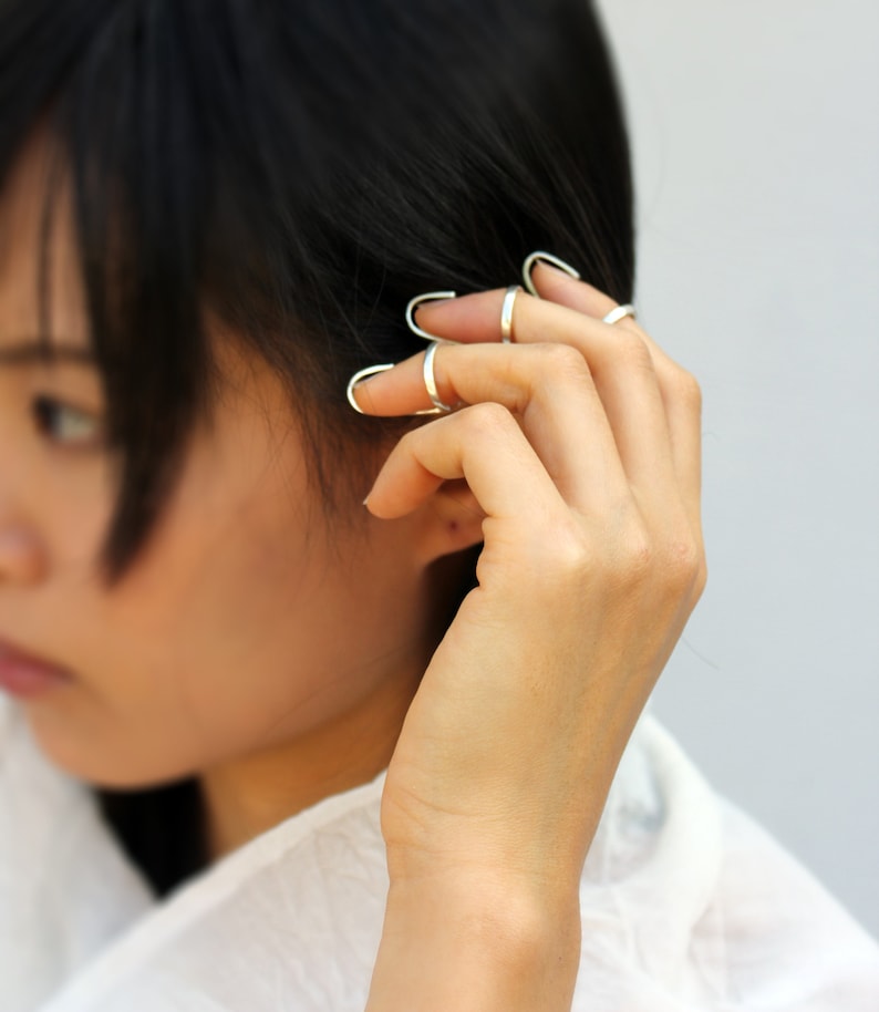 May include: A person wearing multiple silver rings on their fingers. The rings are open and wrap around the finger.