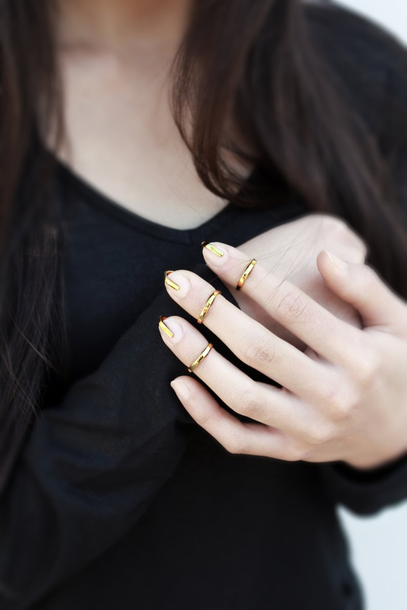 Puede incluir: Primer plano de una mano con anillos dorados en tres dedos. Las u&ntilde;as est&aacute;n pintadas con una combinaci&oacute;n de colores dorados y nude. La persona lleva una camisa negra de manga larga.
