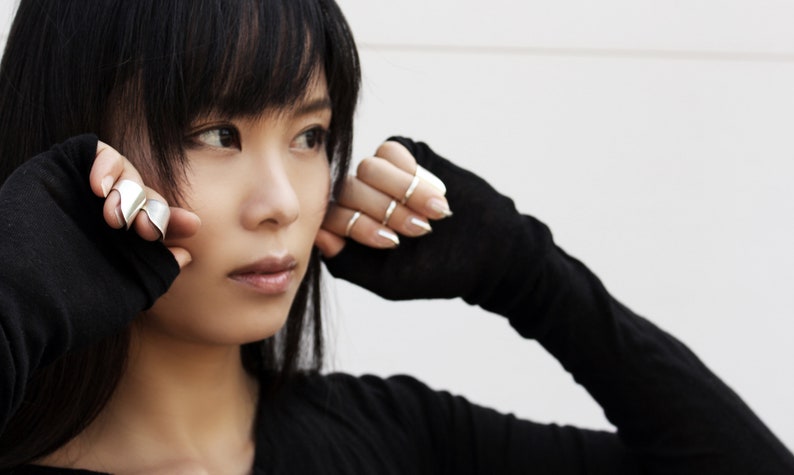 May include: A woman wearing black fingerless gloves with silver rings on her fingers. She is wearing a black long-sleeved shirt.