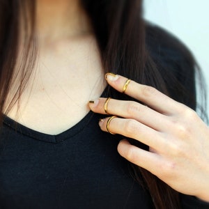 Puede incluir: Anillos dorados en los dedos. Los anillos son finos y sencillos, a&ntilde;adiendo un toque de elegancia. Las u&ntilde;as est&aacute;n pintadas con esmalte de u&ntilde;as dorado. La persona lleva una camiseta negra.