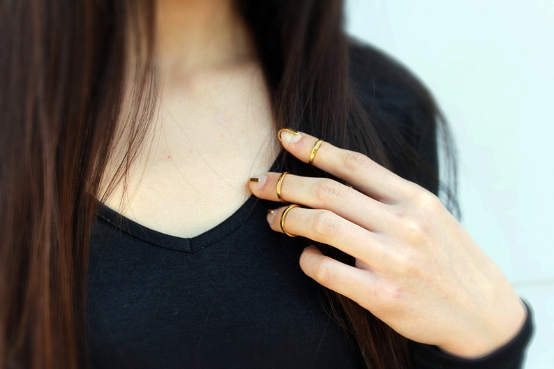Puede incluir: Anillos dorados en los dedos. Los anillos son finos y sencillos, a&ntilde;adiendo un toque de elegancia. Las u&ntilde;as est&aacute;n pintadas con esmalte de u&ntilde;as dorado. La persona lleva una camiseta negra.