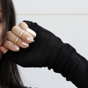 May include: A woman's hand wearing several silver rings on her fingers. The rings are different shapes and sizes, and some are stacked on top of each other. The woman's nails are painted with a silver polish.