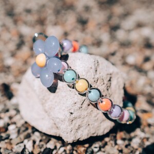 May include: A colorful beaded bracelet with a light blue flower charm. The bracelet is made of pastel-colored beads and has a silver clasp.