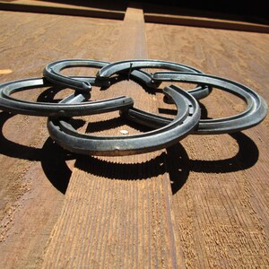 May include: Five silver horseshoes are interlocked to form a decorative design. The horseshoes are arranged in a circular pattern, with the points of the shoes facing outwards. The horseshoes are mounted on a wooden surface.