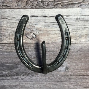 May include: A silver horseshoe with a metal hook attached to the bottom. The horseshoe is mounted on a wooden surface.