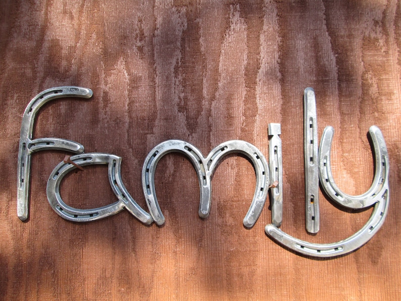 K&ouml;nnte beinhalten: Das Wort "Familie" mit Hufeisen auf einem braunen Holzgrund geschrieben.