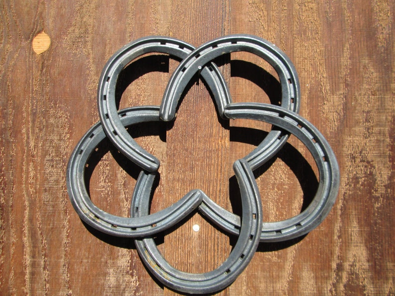 May include: A silver metal horseshoe flower made from six horseshoes intertwined together. The horseshoe flower is on a brown wooden background.