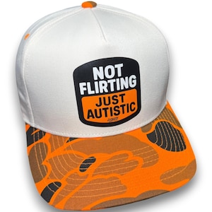 May include: A white baseball cap with an orange button on top and an orange and black camouflage pattern on the brim. The front features a black and orange rectangular patch with the white and orange text: NOT FLIRTING JUST AUTISTIC LUCKLESS.