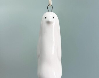 May include: White ceramic penguin ornament with black eyes, hanging from a white string. 5 x 2 cm.