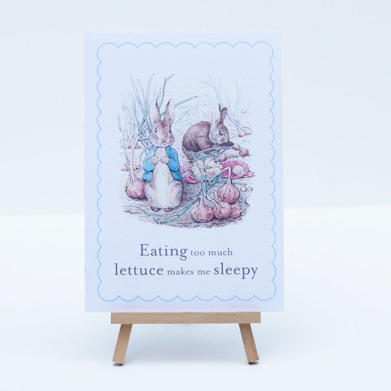 Puede incluir: Una tarjeta azul claro con un borde festoneado presenta una ilustraci&oacute;n vintage de dos conejos en un jard&iacute;n. El texto en la tarjeta dice "Comer demasiada lechuga me da sue&ntilde;o."
