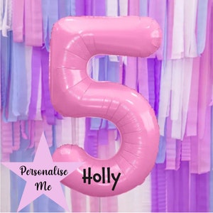 May include: Pink foil number 5 balloon with the name "Holly" written in black on the balloon. The balloon is in front of a background of purple, pink, and blue streamers.