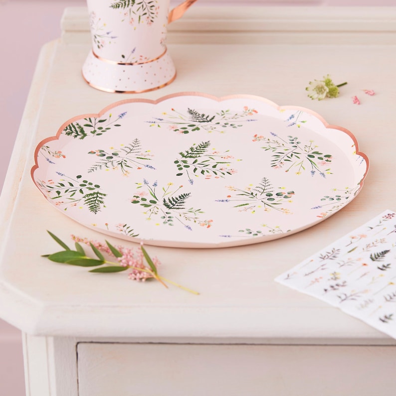 K&ouml;nnte beinhalten: Ein rosa Pappteller mit gewelltem Rand und einem Blumenmuster mit gr&uuml;nen Bl&auml;ttern und rosa Bl&uuml;ten. Der Teller liegt auf einer wei&szlig;en Oberfl&auml;che.