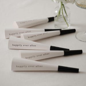 May include: Several white paper cones with black tips are displayed. Each cone is printed with the words "happily ever after". The cones are likely for a wedding or celebration, and are arranged on a white surface.