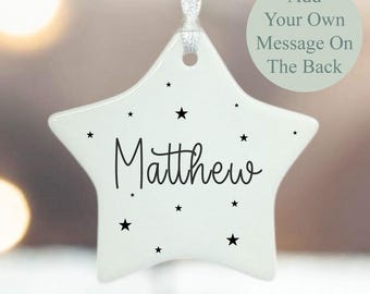 May include: A white star-shaped ornament with the name "Matthew" in black script, surrounded by small black star accents. A ribbon is attached for hanging. The text "Add Your Own Message On The Back" is also present.