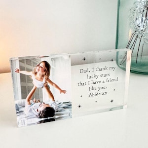 May include: A clear acrylic photo block featuring a photograph of a child being held aloft. The block includes the text "Dad, I thank my lucky stars that I have a friend like you. Abbie xx" and star motifs.