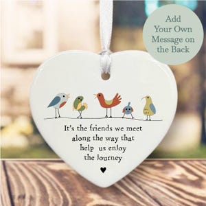 May include: White heart-shaped ceramic ornament with a quote about friendship: "It's the friends we meet along the way that help us enjoy the journey". The ornament features five colourful birds, including a blue bird, a green bird, a red bird, a blue bird, and a yellow bird. The back of the ornament is blank and can be personalised with a message.