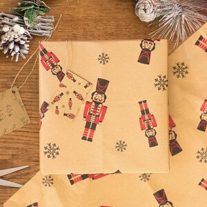 May include: Brown wrapping paper with a repeating pattern of nutcracker soldiers and snowflakes. The nutcracker soldiers are wearing red and black uniforms with gold accents. The snowflakes are black.