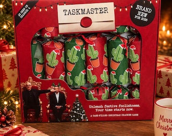 May include: A red rectangular box containing a Taskmaster Christmas cracker game. The packaging features a cactus pattern with Santa hats, the text "TASKMASTER," "AS SEEN ON CHANNEL 4," "BRAND NEW FOR 2026," and "Unleash festive foolishness. Your time starts now."