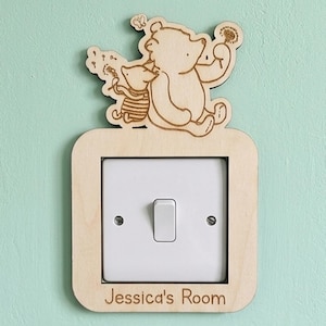 May include: Wooden light switch cover featuring a bear and pig illustration holding dandelions. The cover is rectangular with rounded corners and the text "Jessica's Room" at the bottom. The switch is white and the background is a light green.