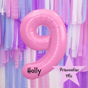 Könnte beinhalten: Rosa Folienballon in Form der Zahl neun mit dem Namen "Holly" darauf gedruckt. Der Ballon befindet sich vor einem Hintergrund aus pastellfarbenen Luftschlangen. Ein rosa Stern mit dem Text "Personalisieren Sie mich" befindet sich in der unteren rechten Ecke des Bildes.