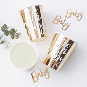 May include: Gold paper cups with white "Oh Baby" text and gold paper cutouts with white "Baby" text.