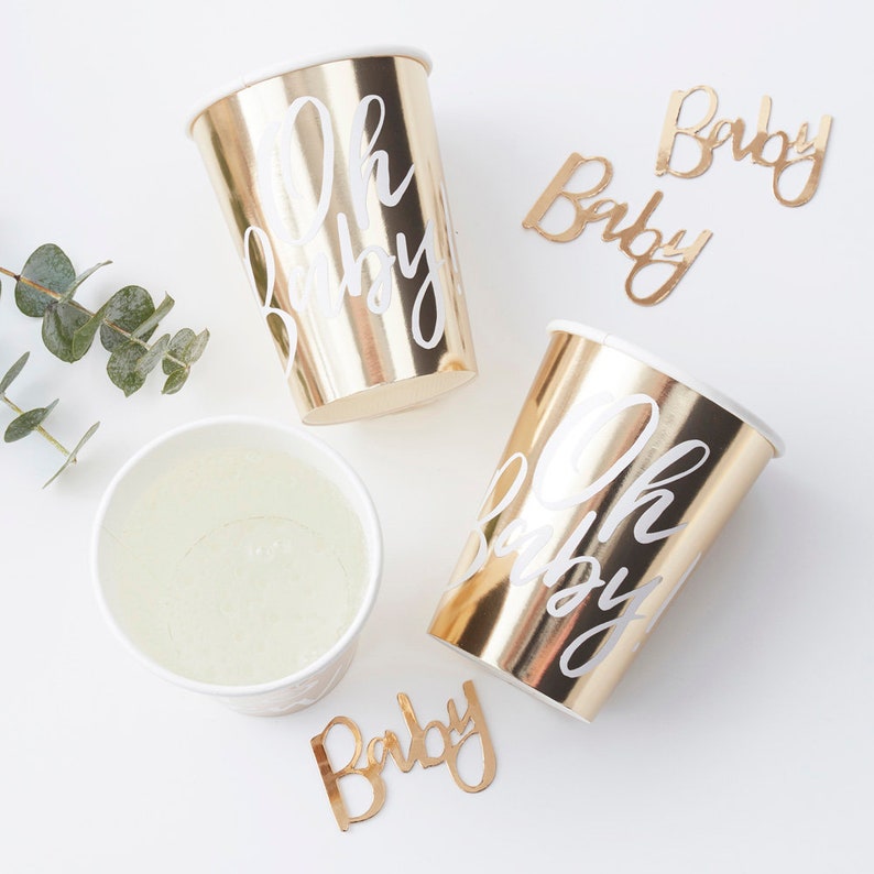 May include: Gold paper cups with white "Oh Baby" text and gold paper cutouts with white "Baby" text.