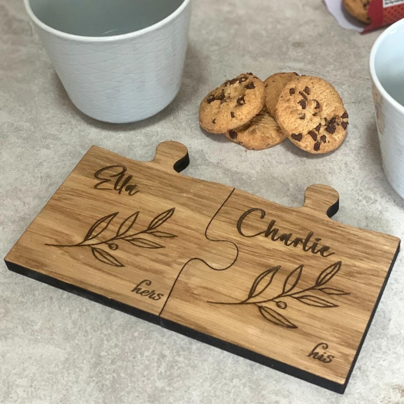 May include: Two wooden puzzle pieces with the names "Ella" and "Charlie" engraved on them. The pieces are joined together and have the words "hers" and "his" engraved on them. The pieces are decorated with a simple branch design.