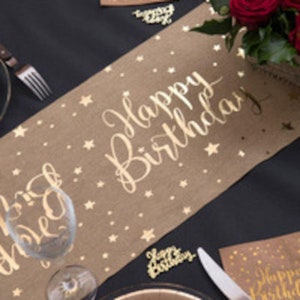 Könnte beinhalten: Ein brauner Tischläufer aus Jute mit goldenen Glitzersternen und dem Schriftzug "Happy Birthday" in goldenen Glitzer.